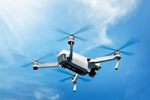 White drone with camera flying in the air over blue sky background