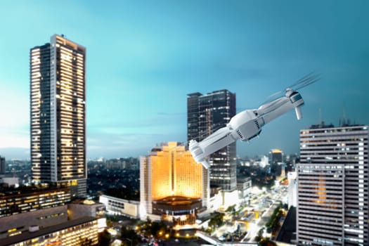 White drone with camera flying above modern city with skyscrapers and lights at night background