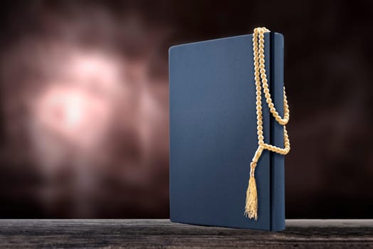 Quran and prayer beads on wooden table over blurry background