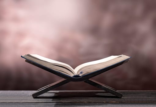 Quran open in wooden placemat on wooden table over blurry background