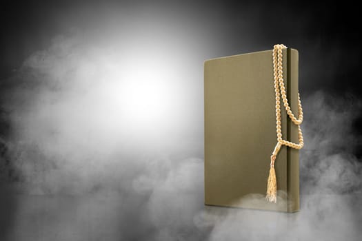 Quran and prayer beads on the table with smoke over black background