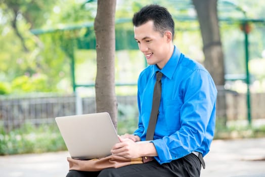 Smiling asian businessman sitting and working with laptop on the park