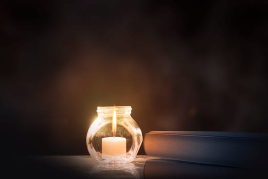 Quran and little candle on wooden table over dark background
