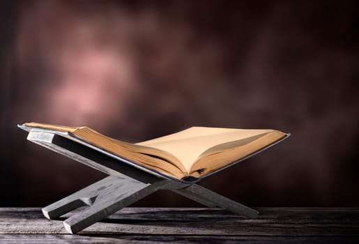Quran open in wooden placemat on wooden table over blurry background