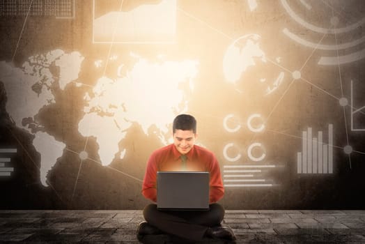 Smiling asian businessman sitting and using laptop with virtual screen which display the interface of financial chart and world maps. Digital technology concept