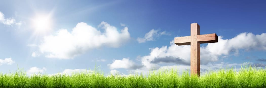 Christian cross on the green grass with sunlight over blue sky background