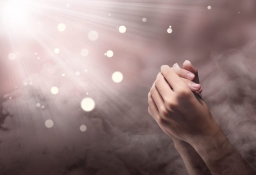 Male hands in praying position with ray over blurry background
