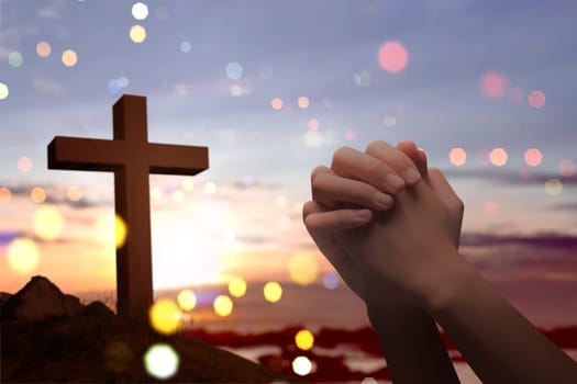 Christian cross and male hands with praying position over sunset background