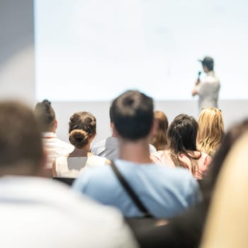 Speaker giving a talk in conference hall at business event. Audience at the conference hall. Business and Entrepreneurship concept. Focus on unrecognizable people in audience.