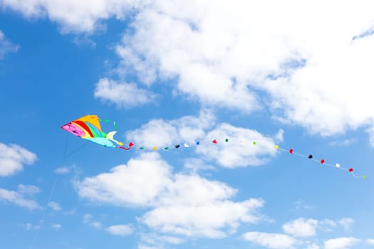 Colorful kite on a blue sky with white clouds.