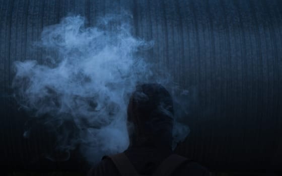 The man smoke an electronic cigarette on the dark background