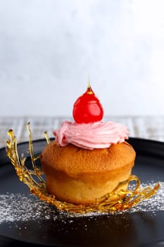 Muffin with cream, cherry and caramel decor on a ceramic plate