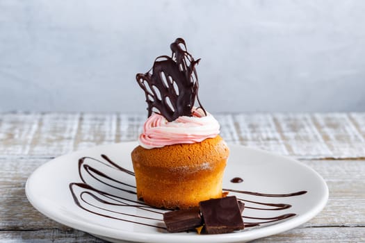 Muffin with cream and chocolate decoration on a ceramic plate