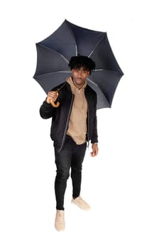 A young African American man in jeans and a sweater standing in the.Studio caring an big black umbrella, isolated for white background.