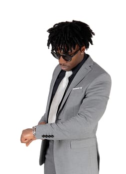 A close up image of an African American man standing in a light gray.suit and black shirt looking at his watch, isolated for white background.