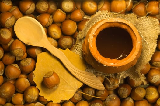 Honey pot with wooden spoon and nuts background
