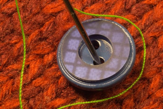 Button and needle with thread on red textile background