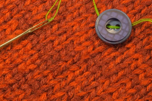 Button and needle with thread on red textile background