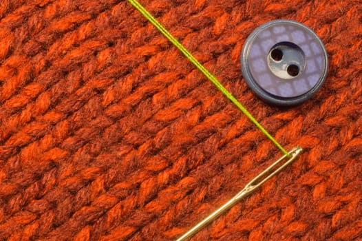 Button and needle with thread on red textile background
