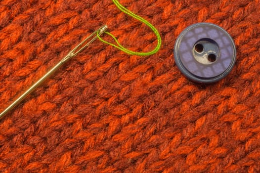 Button and needle with thread on red textile background