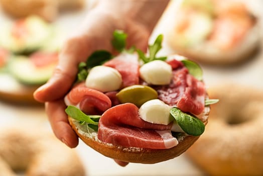 Woman is holding bagel sandwich with prosciutto and mozzareela cheese. Healthy food.