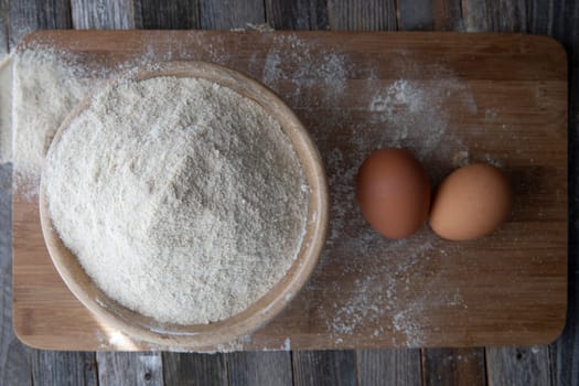 Bowl of whole wheat flour and two eggs on a cutting board.