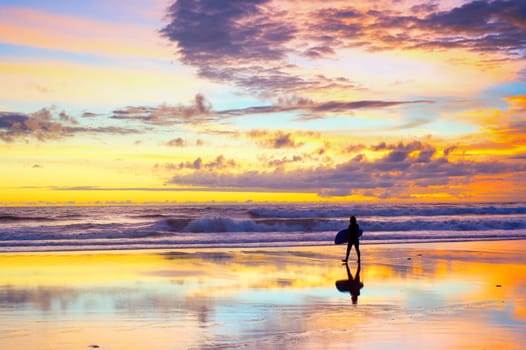 Silhouette of surfer walking by the beach with surfboard at sunset. Bali, Indonesia