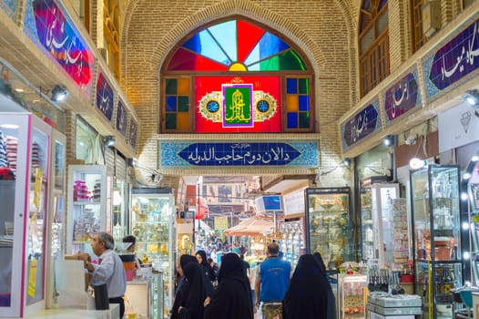 TEHRAN, IRAN - MAY 22, 2017: Crowd of people in row of Grand Bazaar with stalls of dishes. Interior of Grand Bazaar