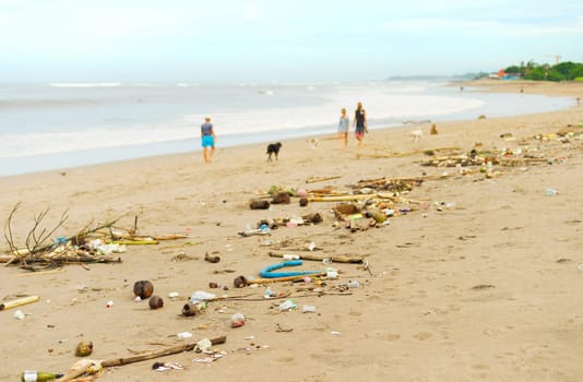 People walking with the dogs by polluted with plastic and waste beach. Bali island, Indonesia