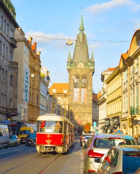 PRAGUE, CZECH REPUBLIC - NOVEMBER 14, 2018: Sunshine in Prague old town street, red tram and car traffic, Henri Bell tower in background
