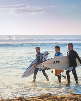 PENICHE, PORTUGAL - OCTOBER 20, 2018: Three boys in wetsuits with surfboards at ocean coast, Peniche, Portugal