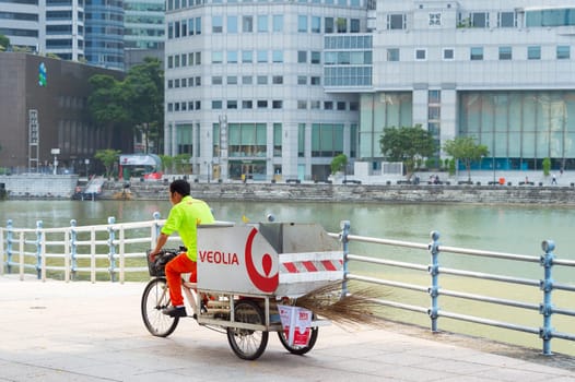 Garbage man service worker riding on bicycle carriage by Singapore downtown embankment