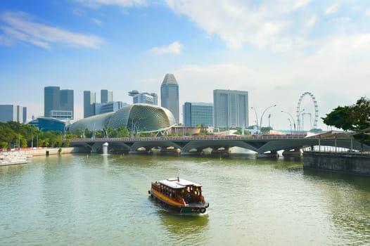 Touristic boat cruise by Singapore Marina bay harbor with ferris wheel flyer, Esplanade Theatres on the Bay and city skyline in background