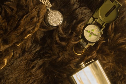 Old steel clock with the compass and the flask on the fur background