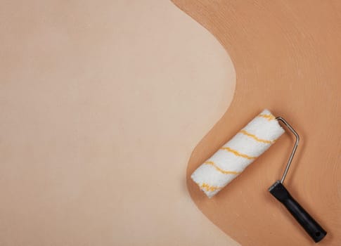 Roller for paint lying on textural double background consisting of two beige shades. Top view with copy space, Concept of construction or design office