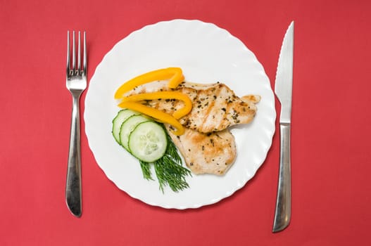 grilled chicken fillet on a white plate and red background