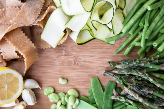 Fresh ingredients for pasta, zucchini, lima beans, green beans, lemon, garlic and homemade whole wheat pappardelle pasta. Flat lay with copy space in center.