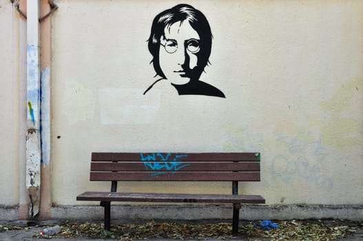 ATHENS, GREECE - AUGUST 30, 2014: Famous musician John Lennon from The Beatles portrait stencil graffiti on textured wall and wooden bench.