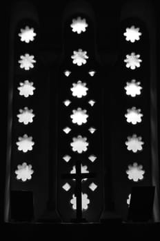 Christian icons and crucifix under arched window in dark church interior. Black and white.