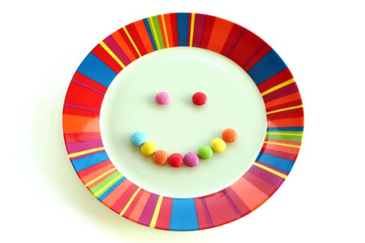 Smiling face made from candy and colorful plate on white background. Kids dessert food happy meal.