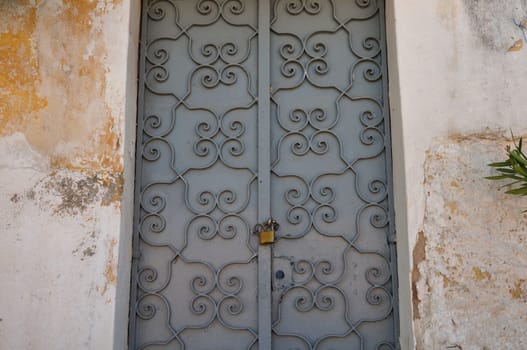 Iron gate with old fashioned metalwork pattern and textured wall background. Abandoned house exterior.