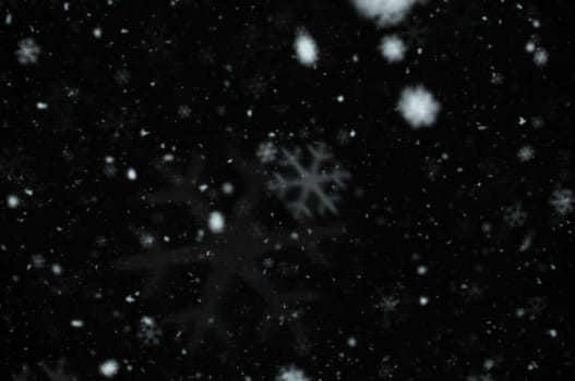 Snow falling on dark winter night. Snowflakes bokeh effect abstract blur.