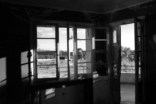 Sunlight shining through broken window and door in abandoned house. Black and white.