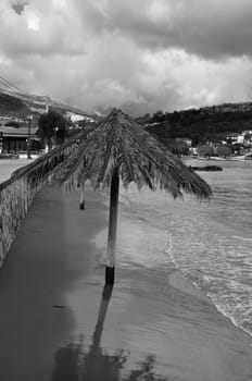 Sandy beach in the wintertime and parasol with palm tree leaves. Black and white.