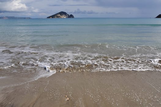 Waves splashing on sandy beach Keri in Zakynthos Greece and Marathonisi island natural habitat of the caretta-caretta sea turtle.