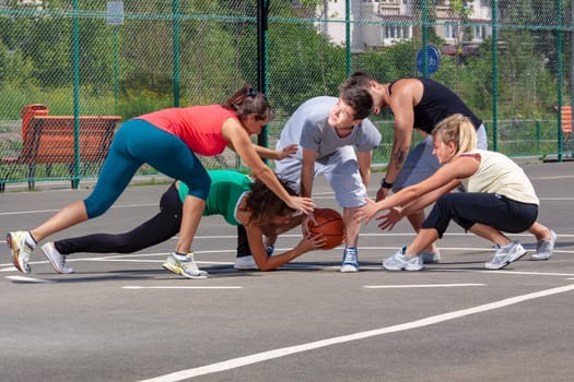 Mixed young people, men and women, playing basketball on a playground