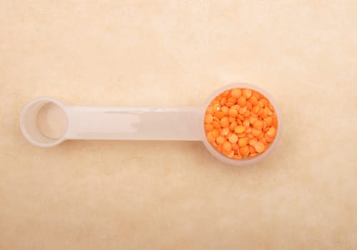 Red lentils on measuring spoon and brown background