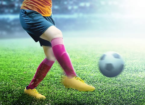 Football player woman in orange jersey kicking the ball on the football field