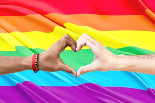 Couple of gay making a heart sign by hand with rainbow flag background. LGBT concept