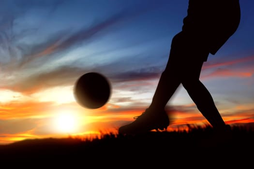 Silhouette of football player woman kicking the ball on the grass field with sunset view background